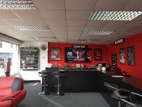 Inside the Leyland shop: a black counter with bar stools under a 'Fluid Bar' sign, red walls and a red sofa by the window